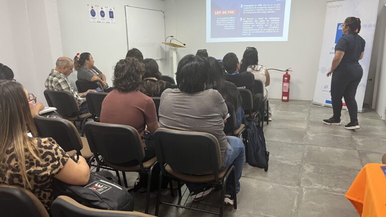 Personas trabajadoras a honorarios participan en una jornada de capacitación sobre Seguridad y Salud en el Trabajo, mientras una expositora presenta contenidos sobre la Ley 16.744