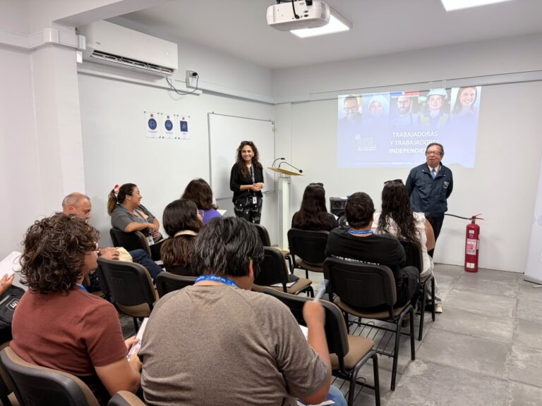 Personas trabajadoras a honorarios participan en una jornada de capacitación del ISL sobre Seguridad y Salud en el Trabajo, mientras dos expositores presentan contenidos frente al público.