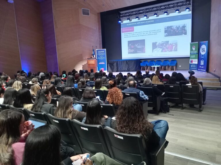 Personas asisten a una jornada sobre salud mental y prevención de riesgos psicosociales, mientras una expositora realiza una presentación desde el escenario ante un auditorio.